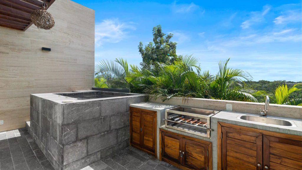 Modern outdoor kitchen space with stone barbecue, wooden cabinets and sink